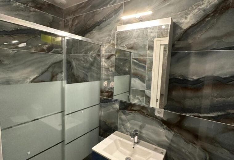 Salle de bain moderne carrelée en marbre foncé (gris/bleu), avec douche à paroi vitrée dépolie, meuble-lavabo bleu nuit avec vasque blanche et meuble miroir.